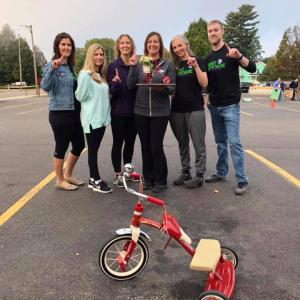Team of six people posing with trophy and tricycle 